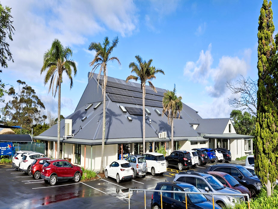Community centre building with distinctive peaked roof and palm trees, car park in foreground