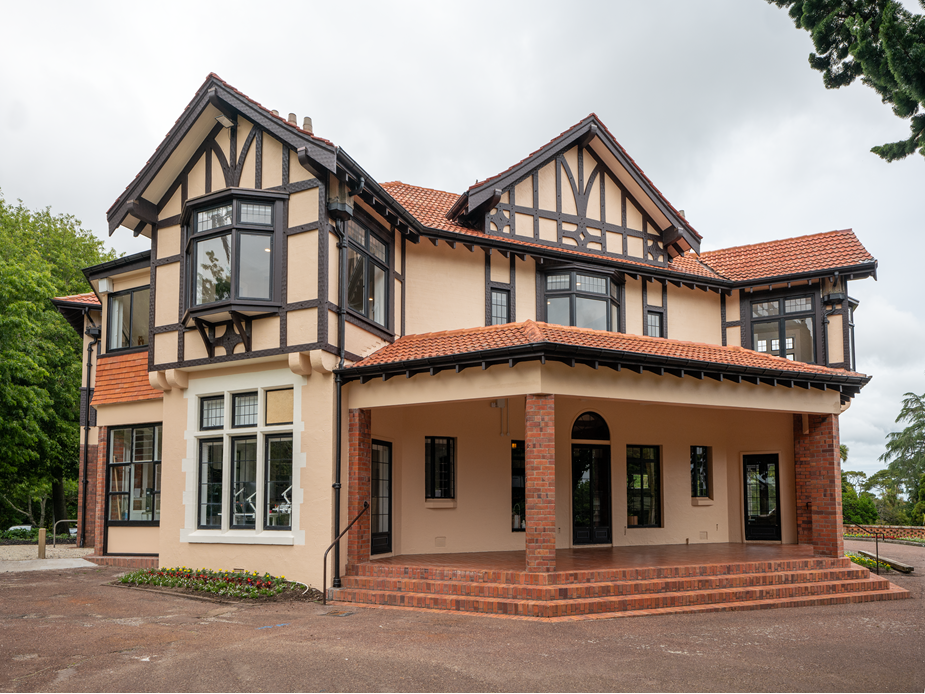 Two-storey cream and red-brick Tudor-revival homestead with terracotta tile roof, covered entrance porch