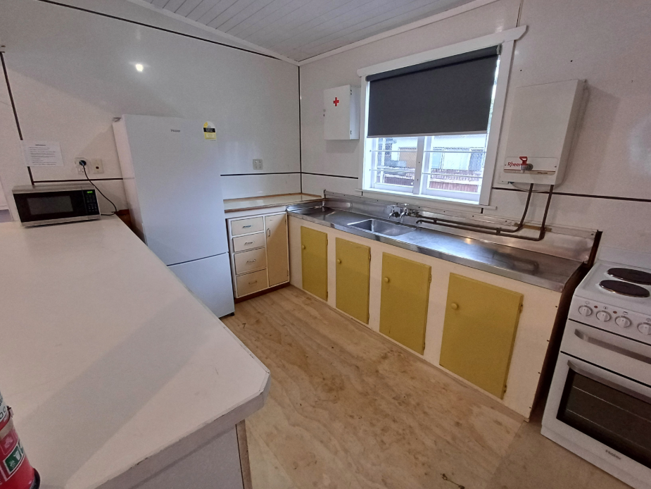 Basic kitchen with yellow cabinets, stainless bench and white appliances