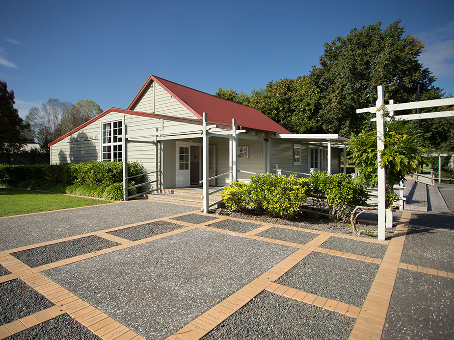 White weatherboard hall with red roof, covered veranda, and gravel forecourt