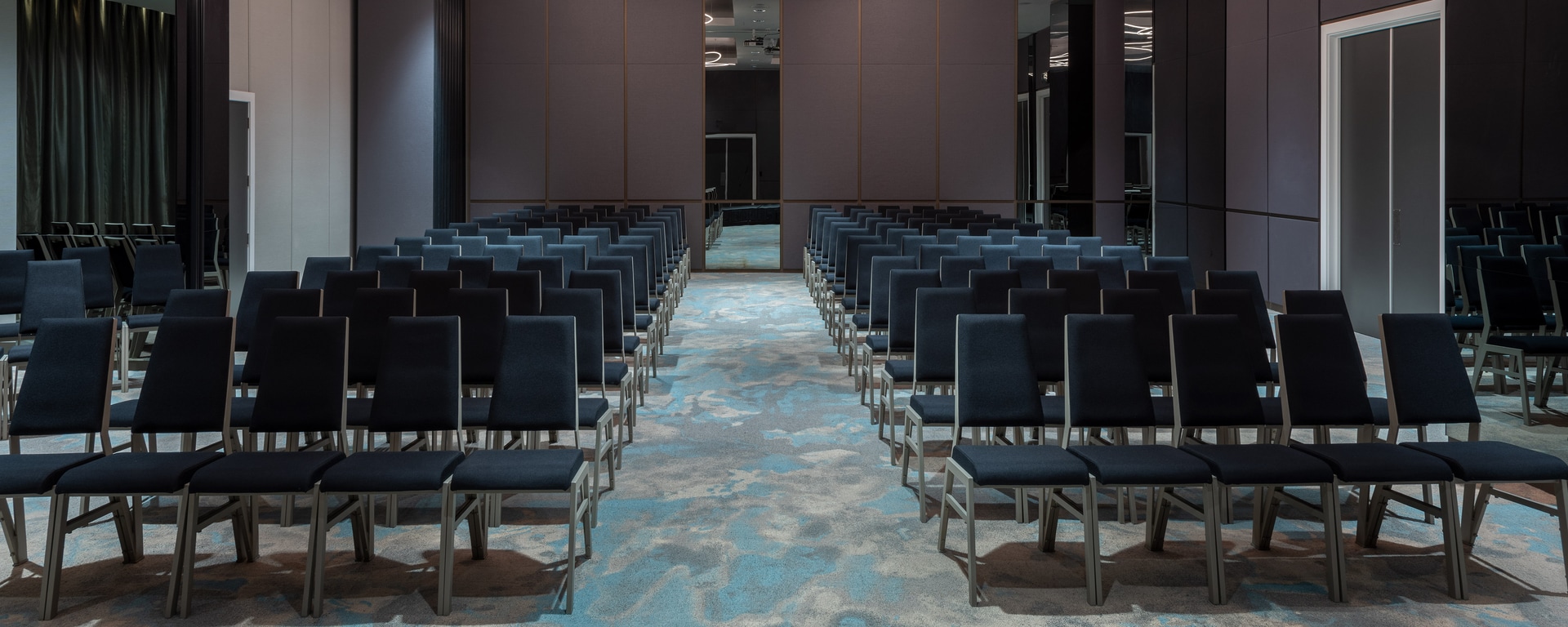 Hotel ballroom in theatre layout with rows of dark chairs and decorative lighting