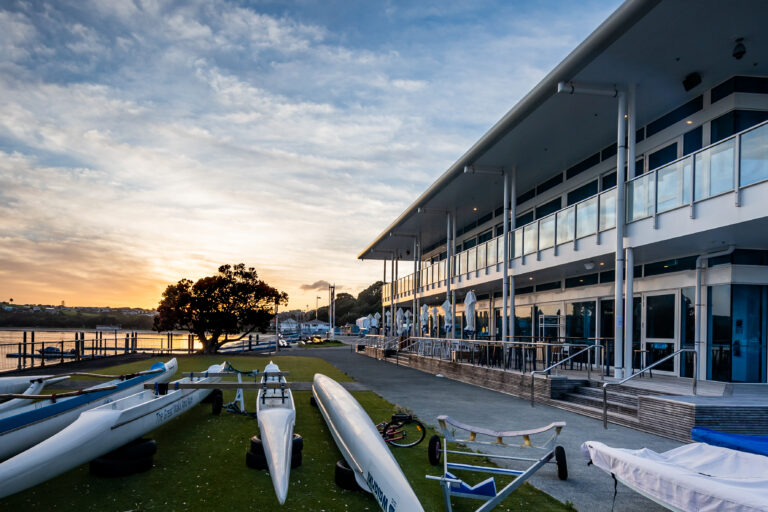 Two-storey waterfront function centre at sunset with boats on the foreshore