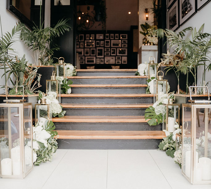 Staircase decorated with lanterns, white flowers and trailing greenery in a venue entrance