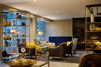 Hotel lounge with yellow and brown armchairs, open shelving with decorative objects, blue patterned wall panels