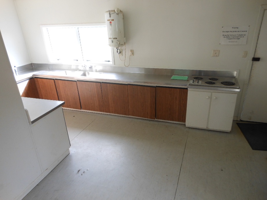 Basic hall kitchen with stainless bench, timber base cabinets, and wall-mounted hot water unit