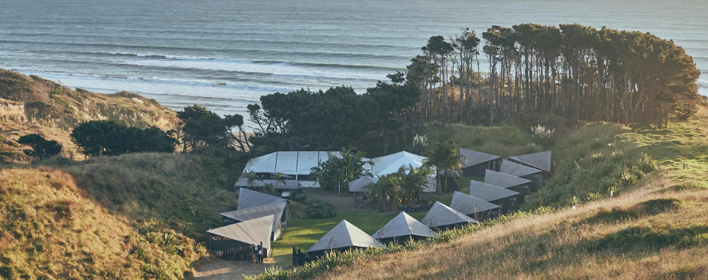 Aerial view of coastal retreat with tent structures on hillside above beach