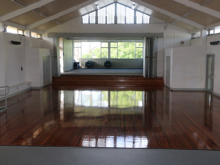 Hall interior with vaulted ceiling, polished timber floor, and raised platform seen from the stage end