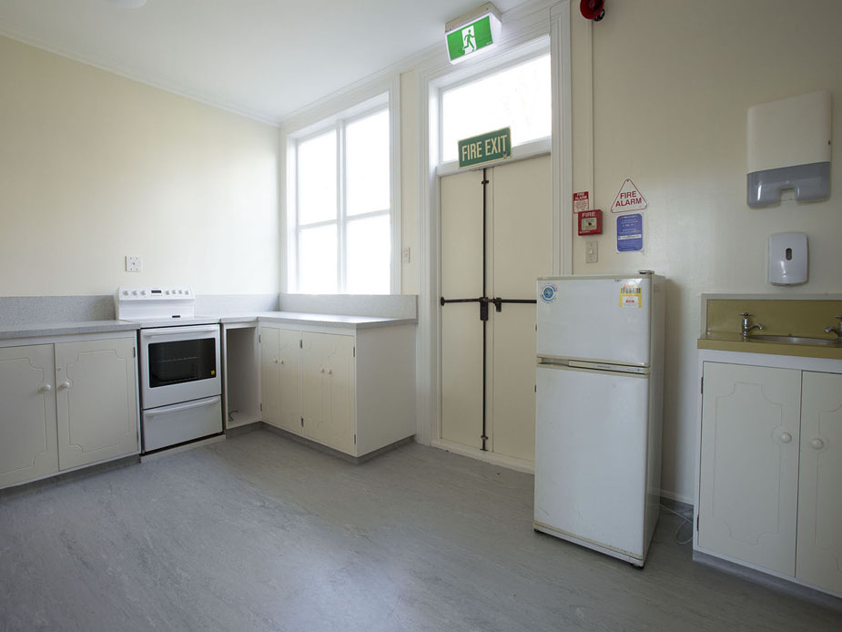 Basic cream kitchen with white stove, fridge, cabinets, and vinyl floor, fire exit door visible