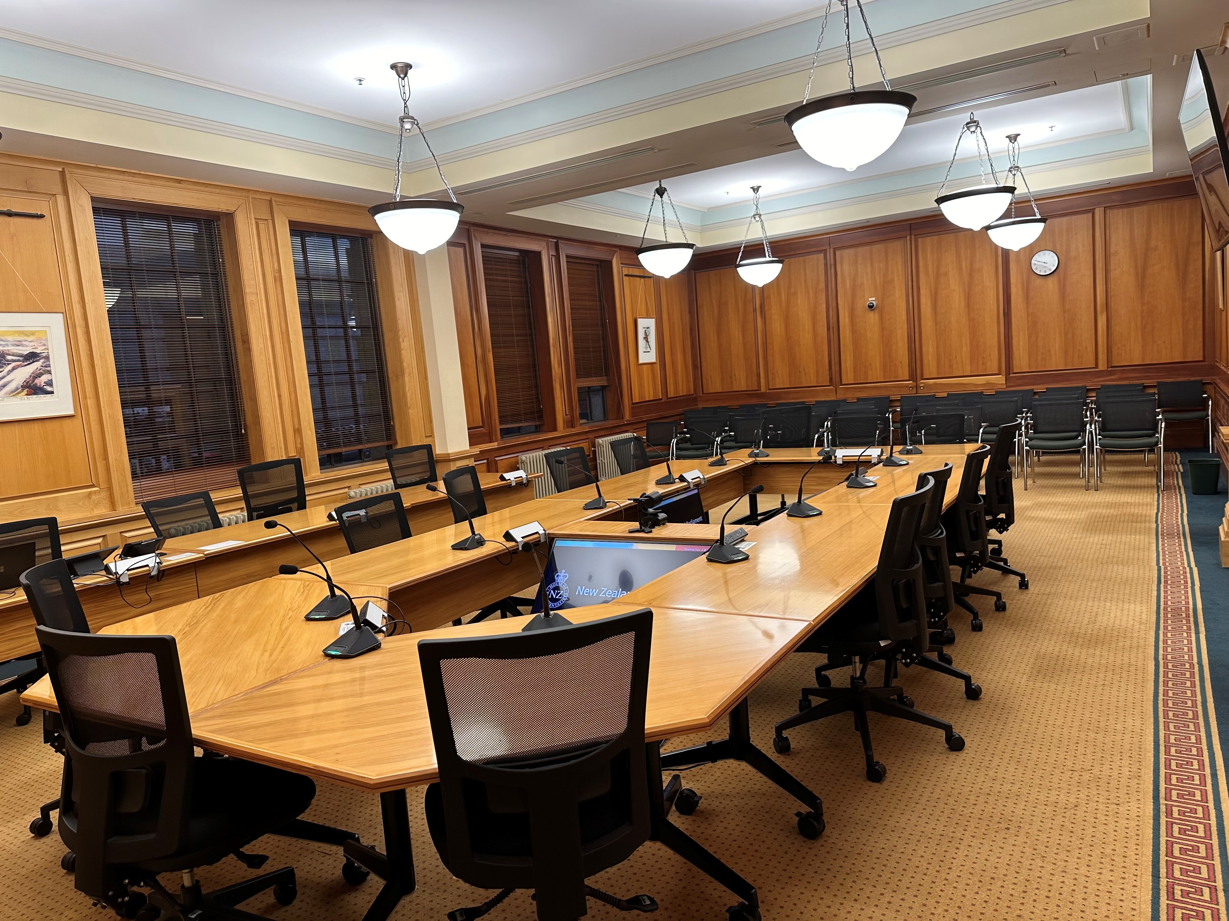 Formal meeting room with timber-panelled walls, large oval table, microphones and pendant lights