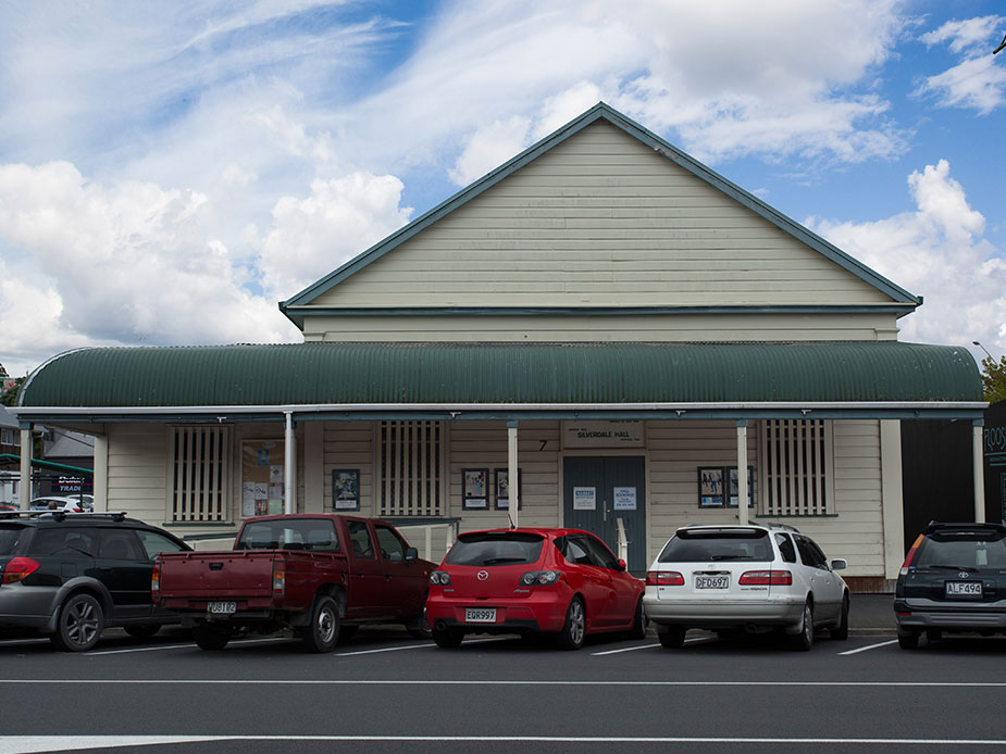 Weatherboard hall building with green roof and cars parked in front