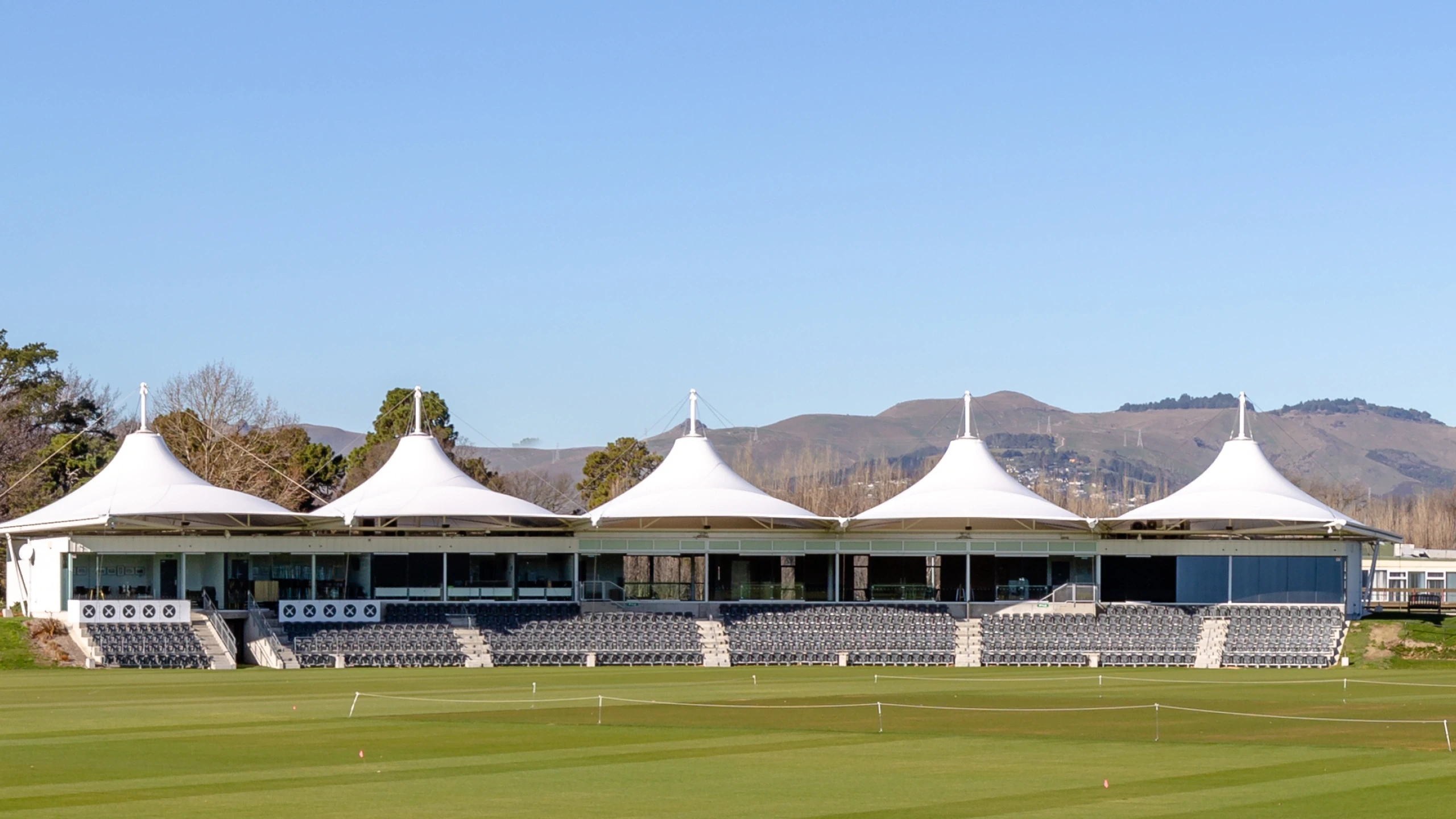 Cricket oval grandstand with distinctive peaked white canopy roofs and hills behind