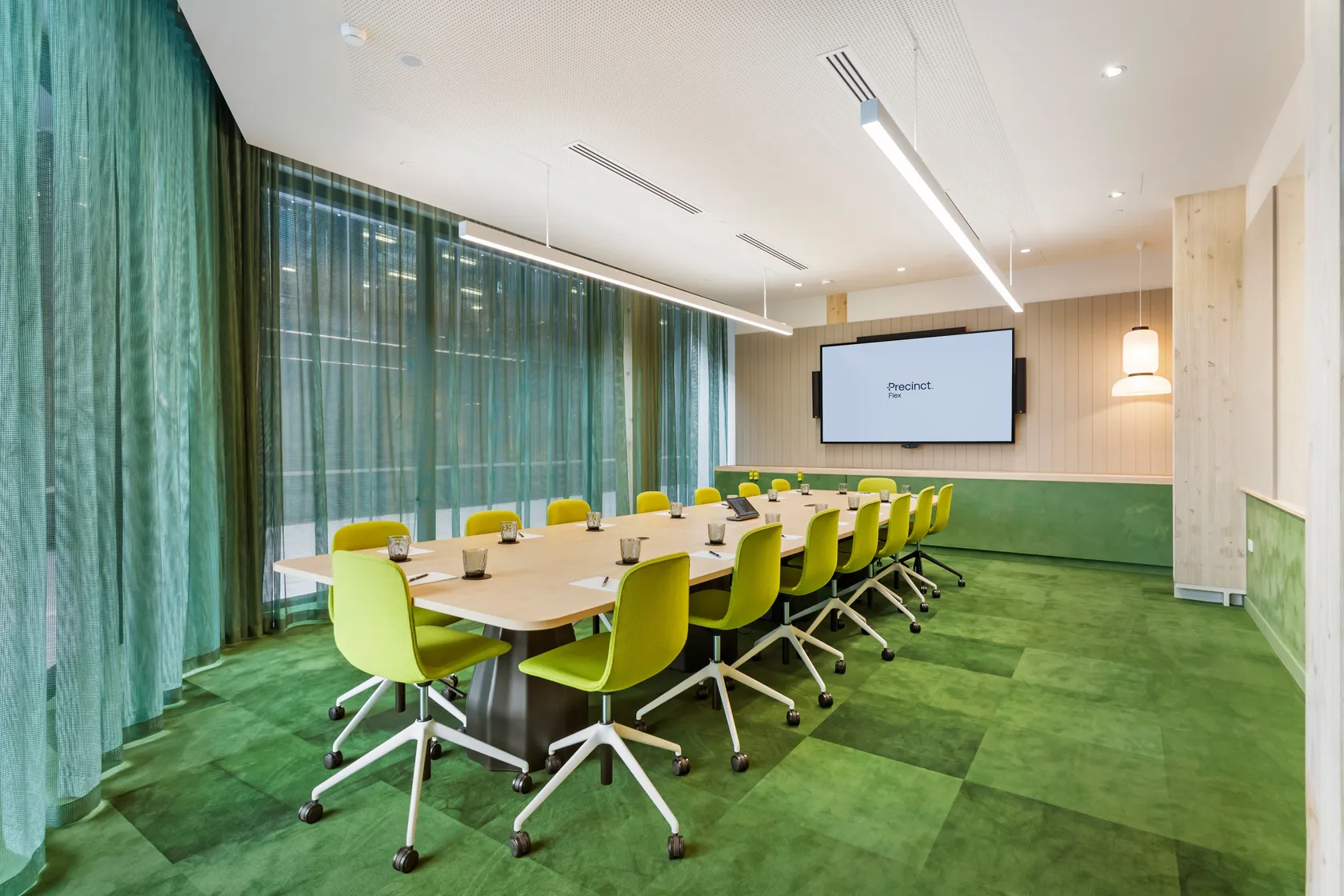 Meeting room with long timber table, green chairs, green carpet and large wall-mounted screen
