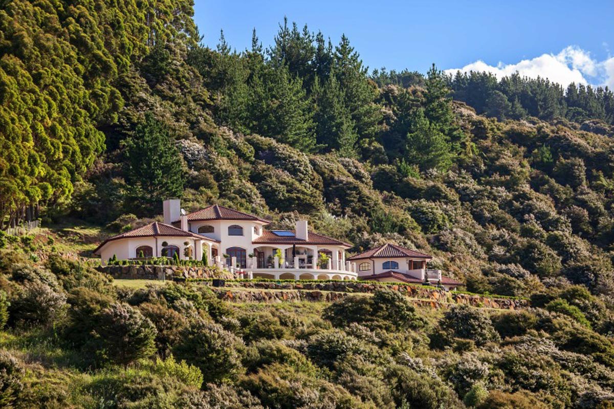 The full Mediterranean-style building seen from the hillside in daylight, set into forested slopes