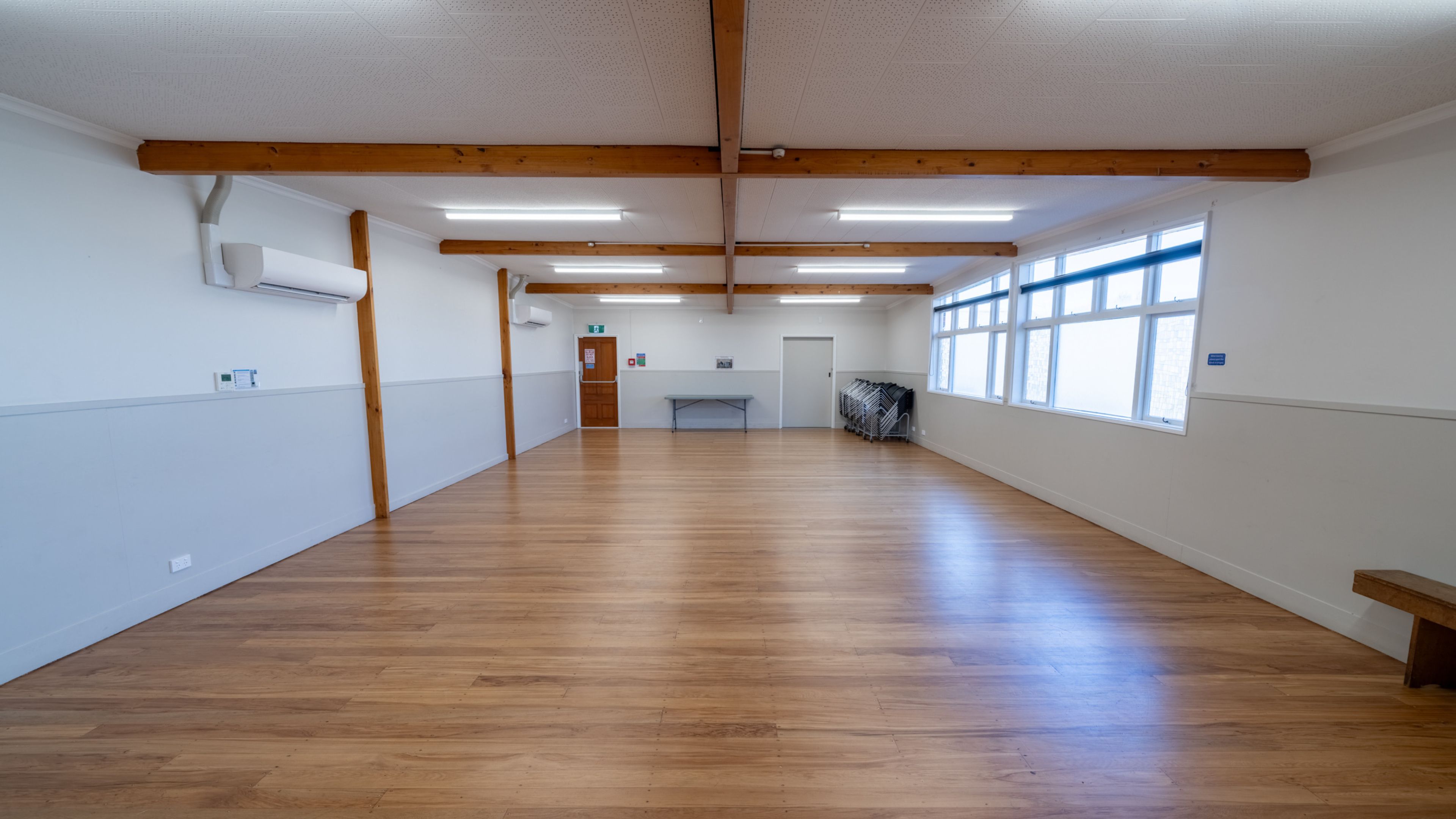 Empty hall with timber floor, exposed beams and natural light from high side windows