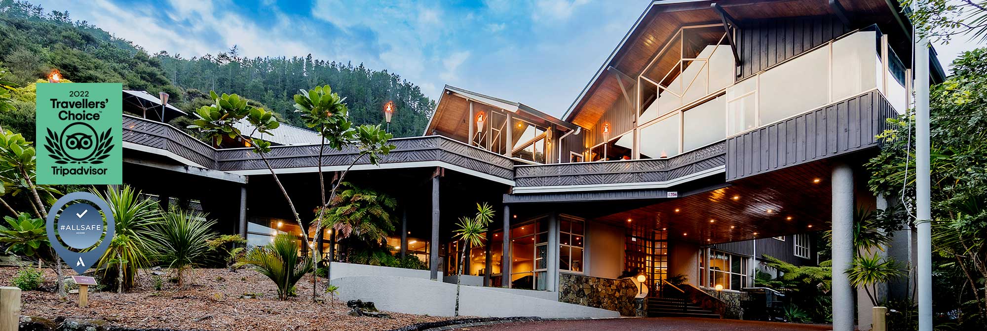 Multi-level resort building with decks lit at dusk amid trees