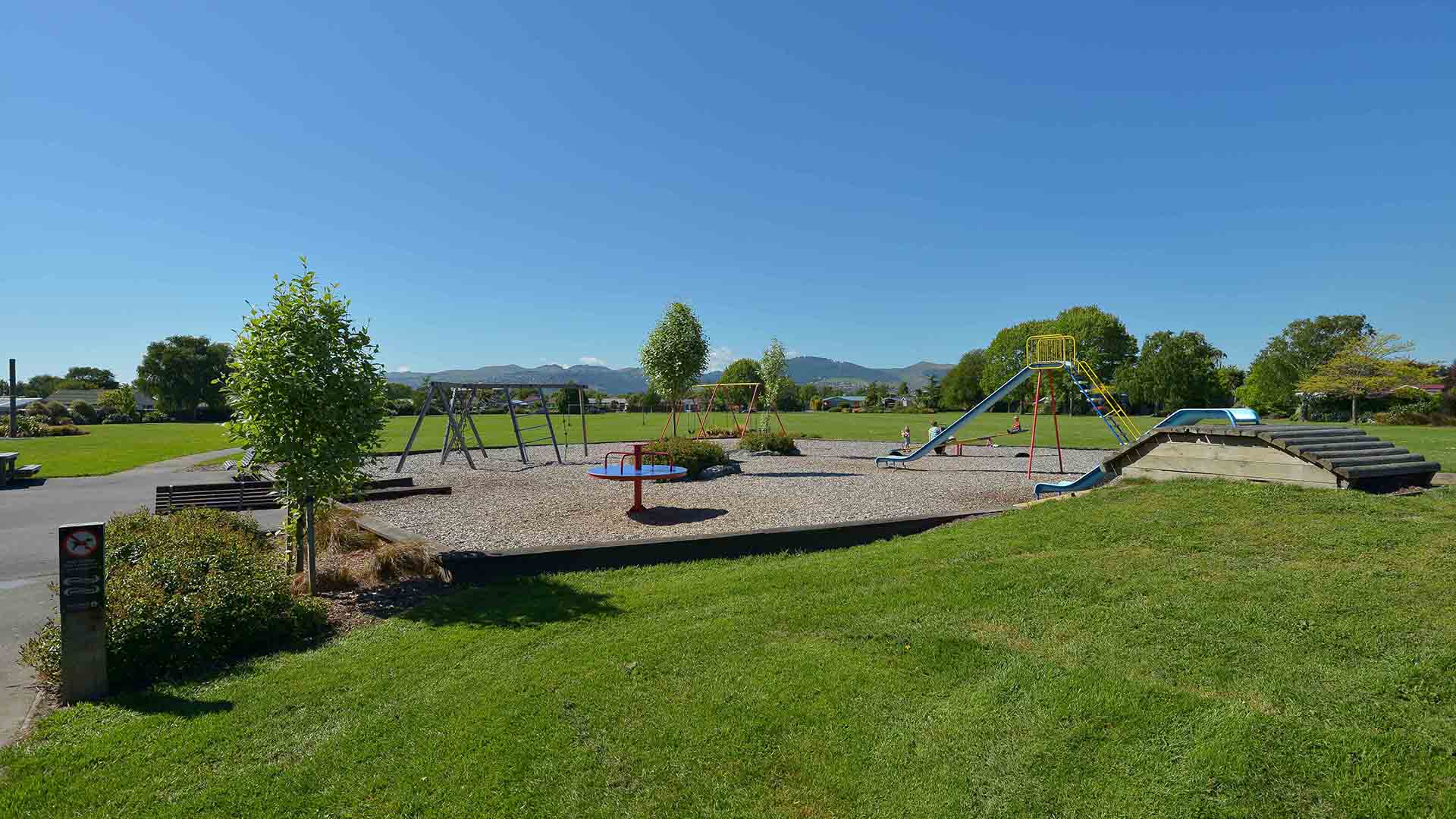 Open park with playground equipment, trees and mountain backdrop