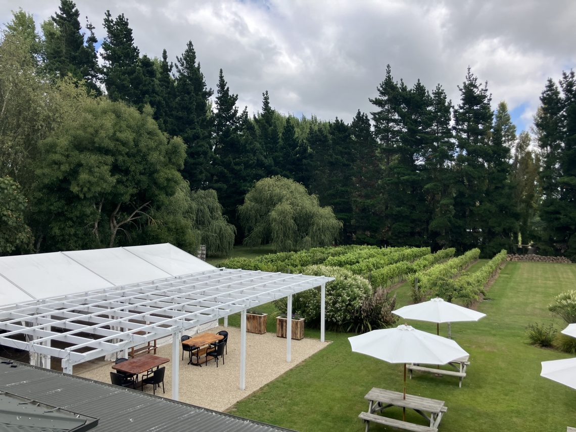 Outdoor venue grounds with marquee structure, pergola, lawn, and trees