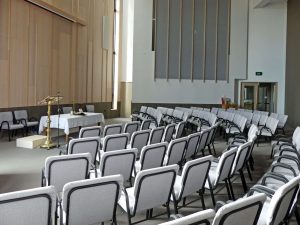 Church sanctuary set with rows of chairs for an event, altar and stained glass at far end