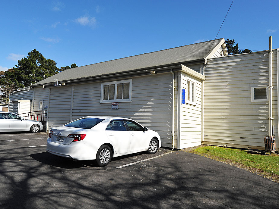 Side view of weatherboard hall with car park and trees