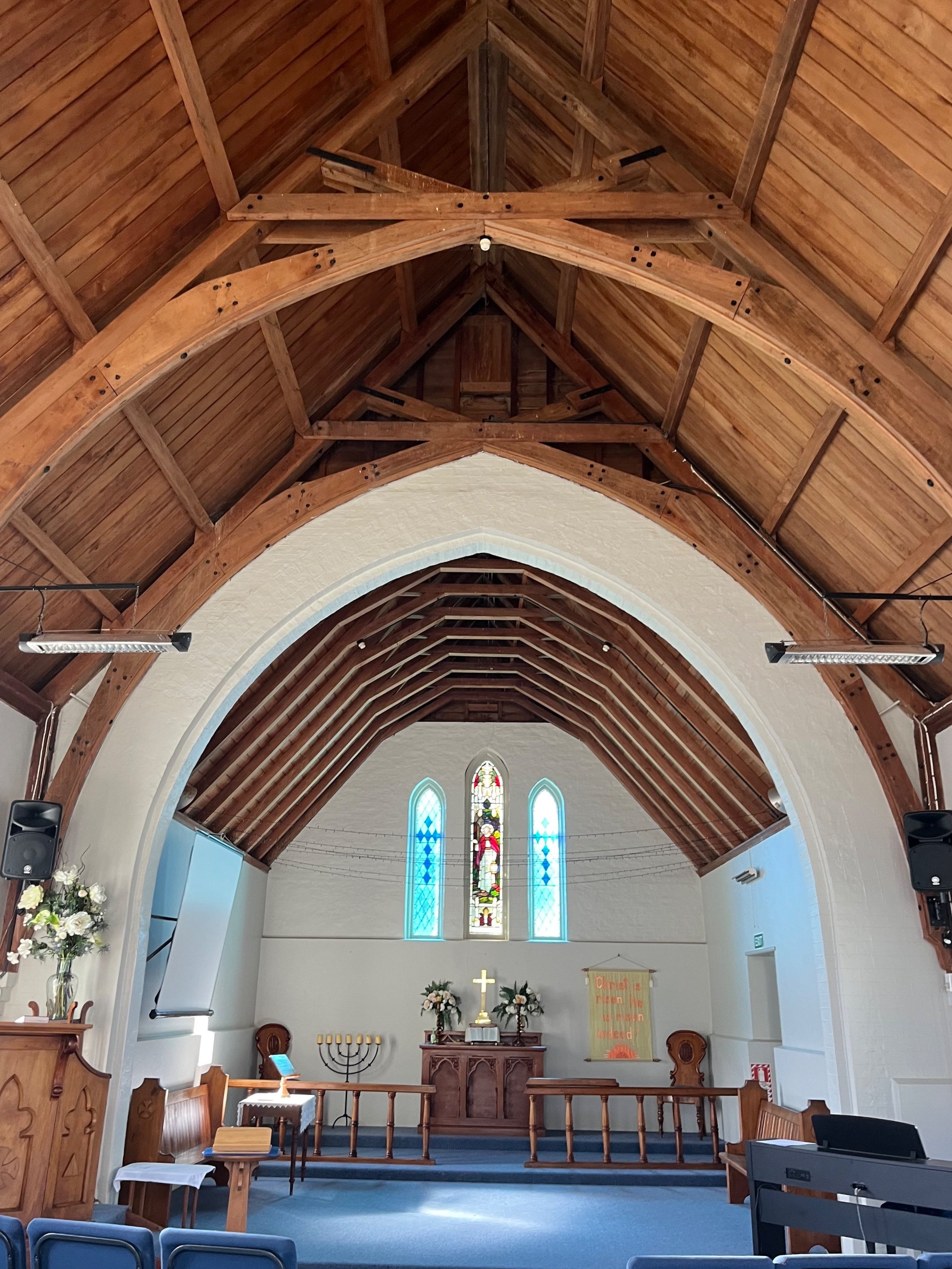 Church interior with timber vaulted ceiling, arched nave, stained glass windows, and altar