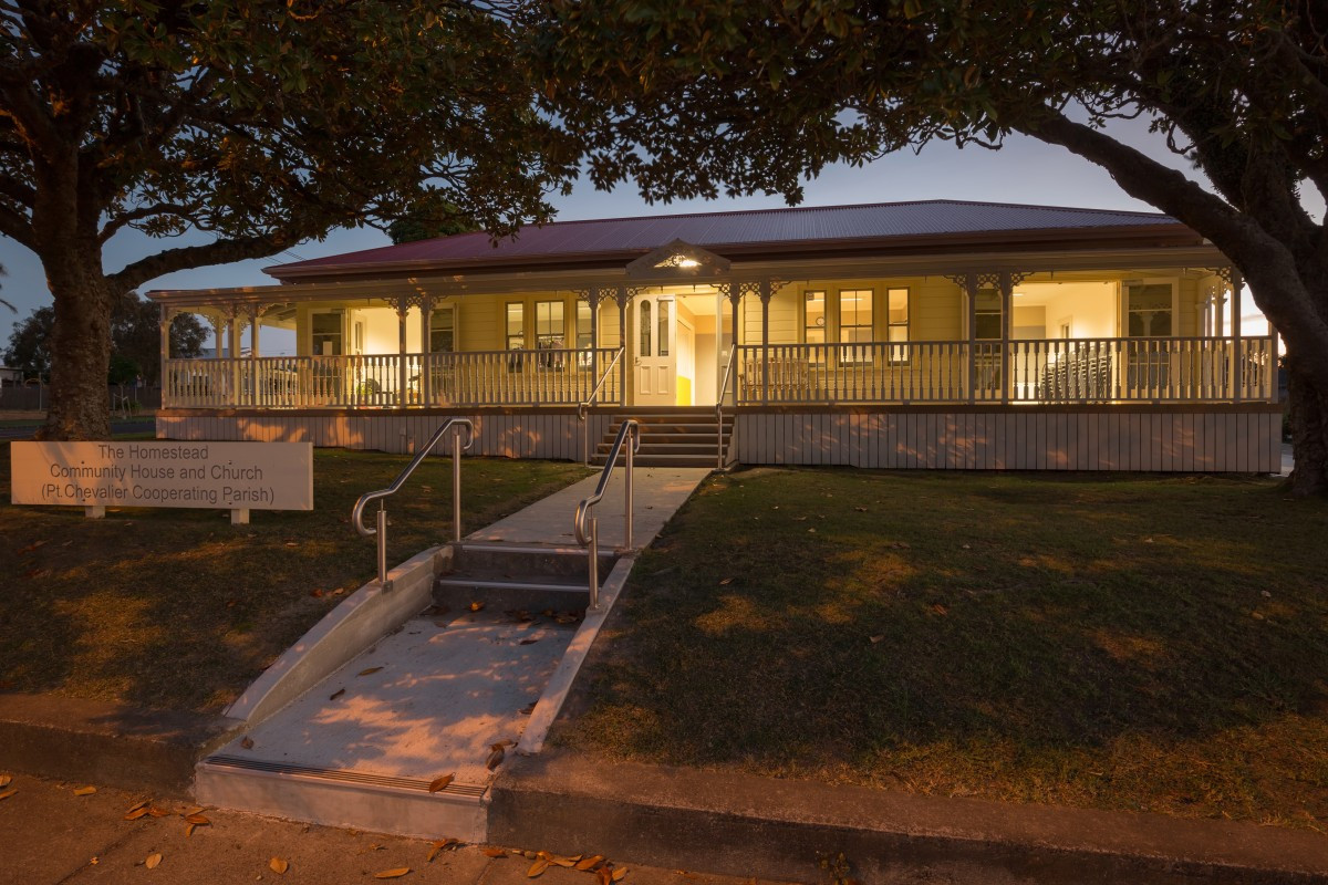 Illuminated heritage villa-style building at dusk with verandah and signage, trees framing