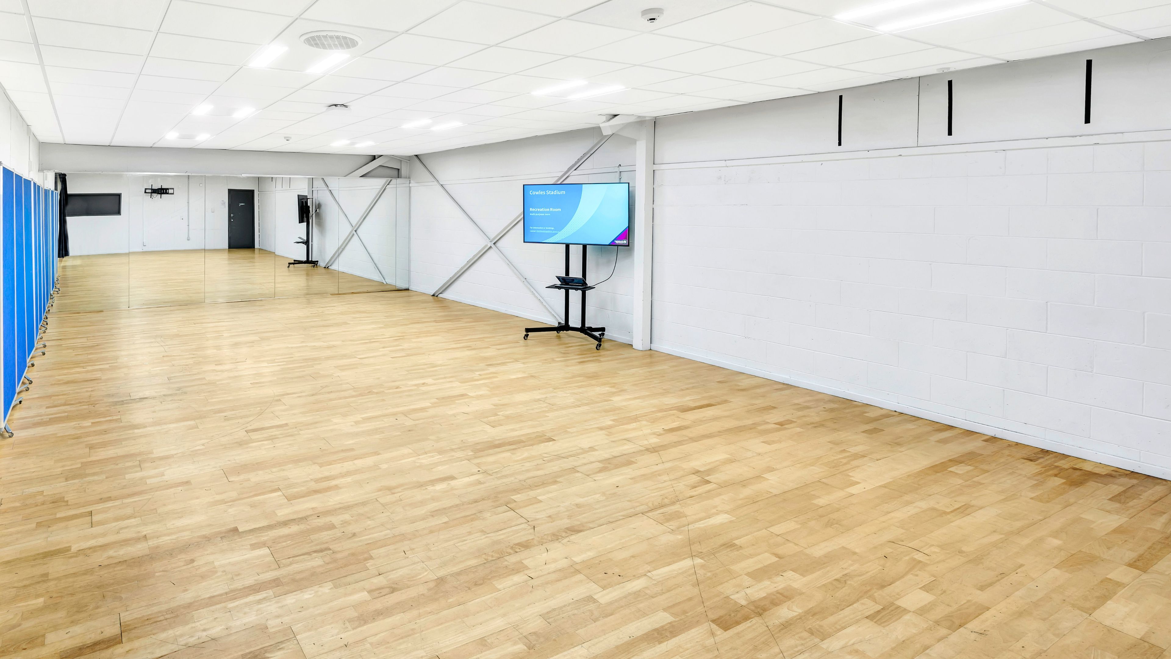 Plain rectangular hall with timber floor, wall mirrors, and a freestanding screen