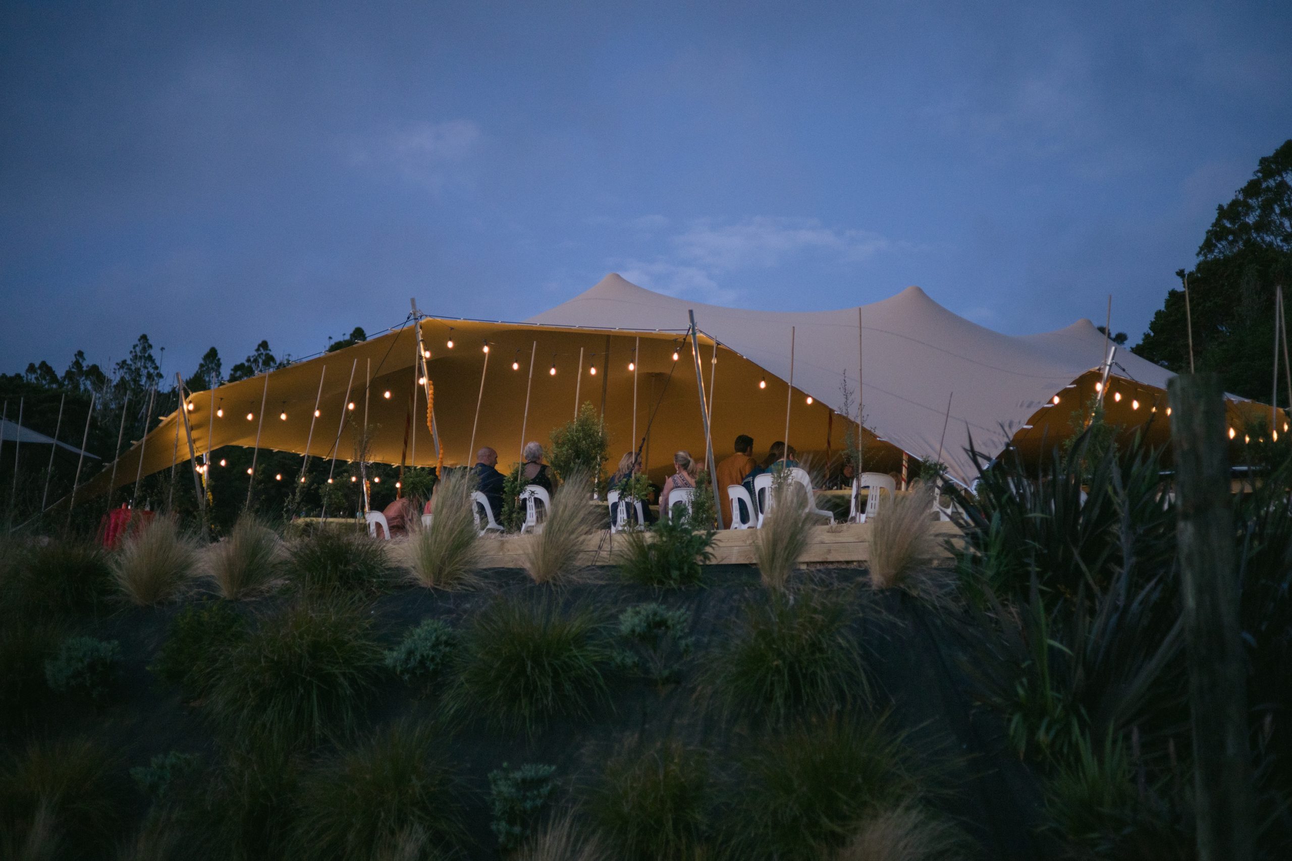 Illuminated stretch tent on hillside with guests seated at dusk