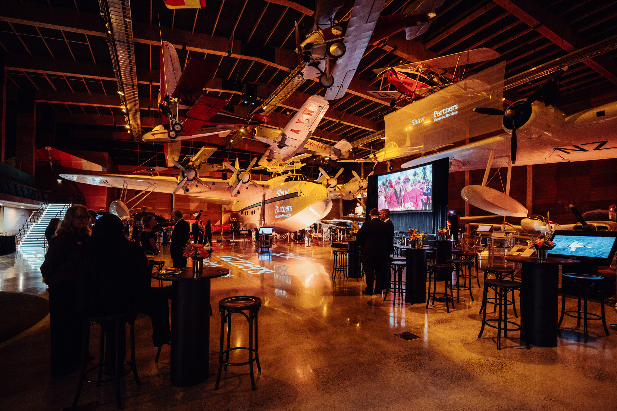 Event space inside a museum hall with vintage aircraft suspended overhead and cocktail tables
