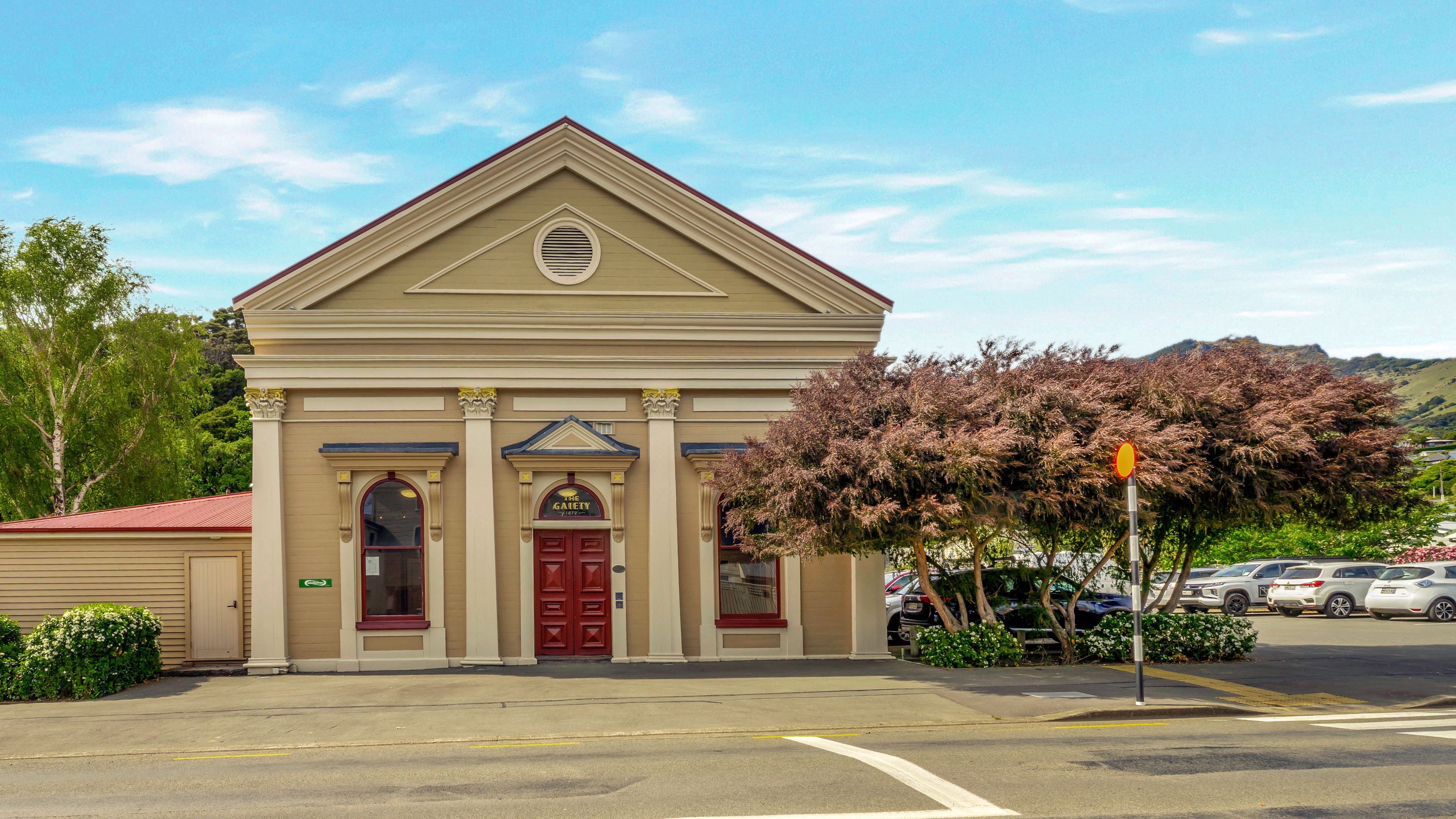 Cream rendered heritage building with classical columns, triangular pediment, red double doors