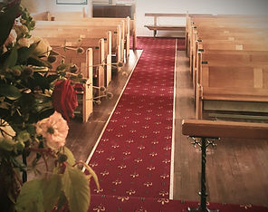 Church interior with timber pews, red carpet aisle and flower arrangements