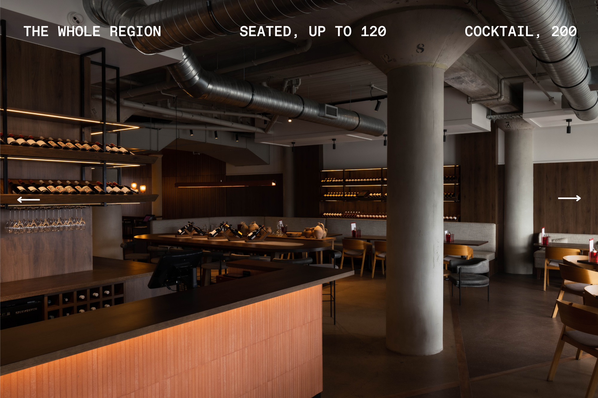 Industrial-style dining room with concrete columns, backlit wine racks, and timber banquettes