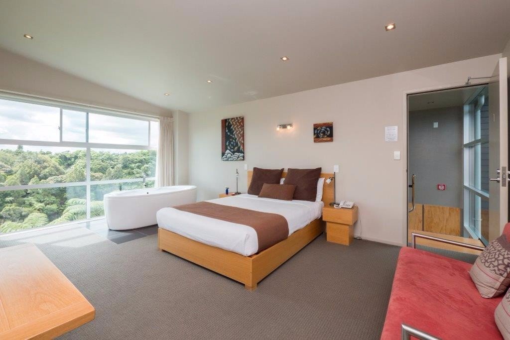 Studio with a king bed and a freestanding bath beside full-height windows over native bush