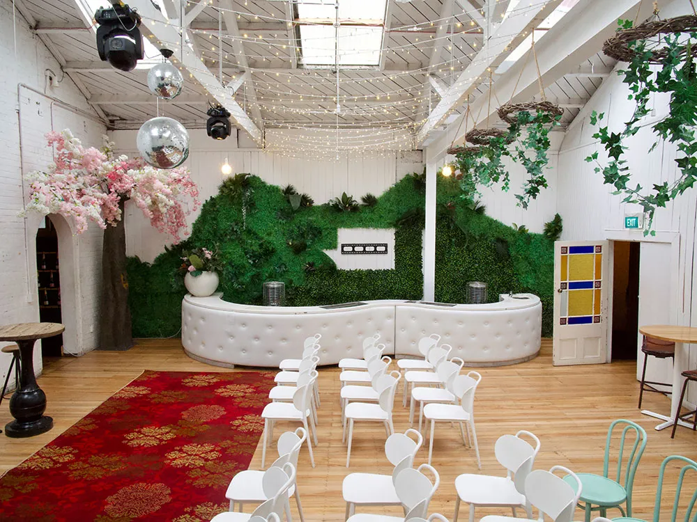 White-painted industrial hall with living green wall, white curved bar, and disco balls above