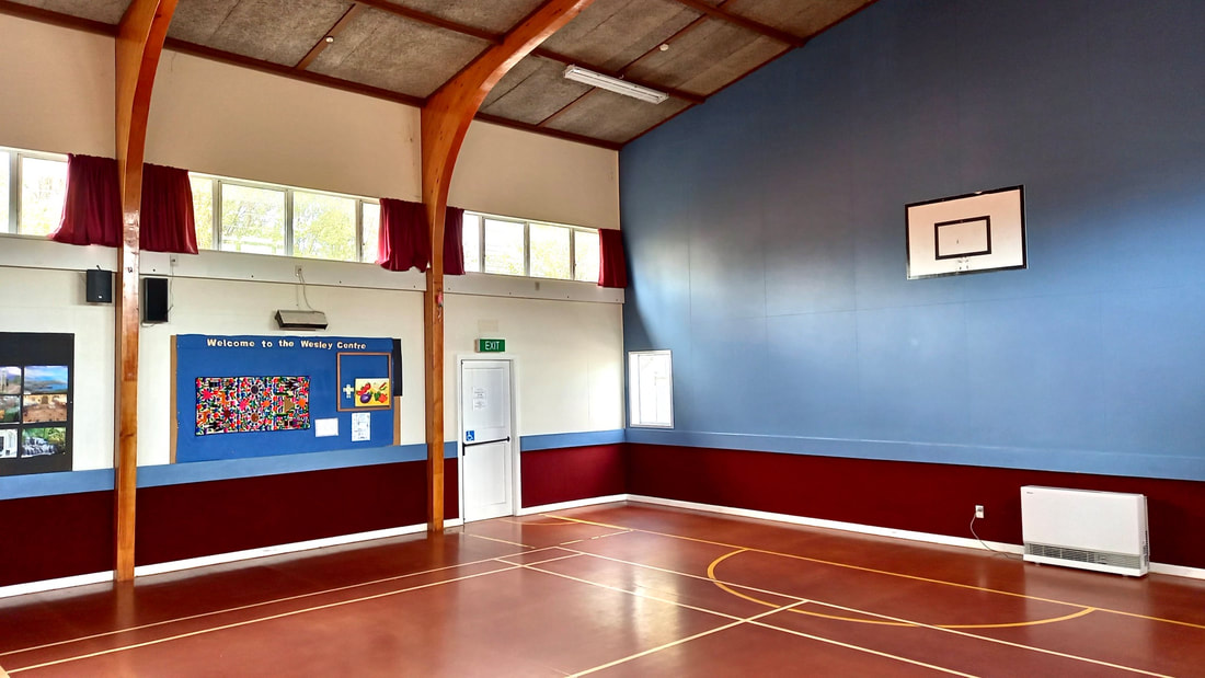 Multi-use hall interior with timber-arch portal, blue and red painted walls, and court markings
