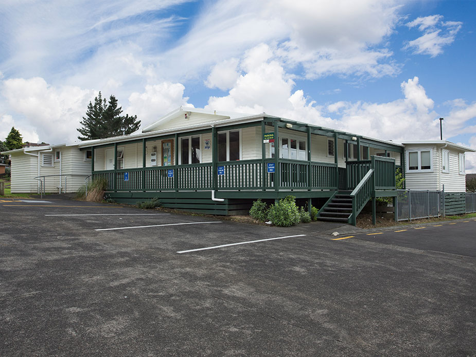White weatherboard community house building with green veranda and car park
