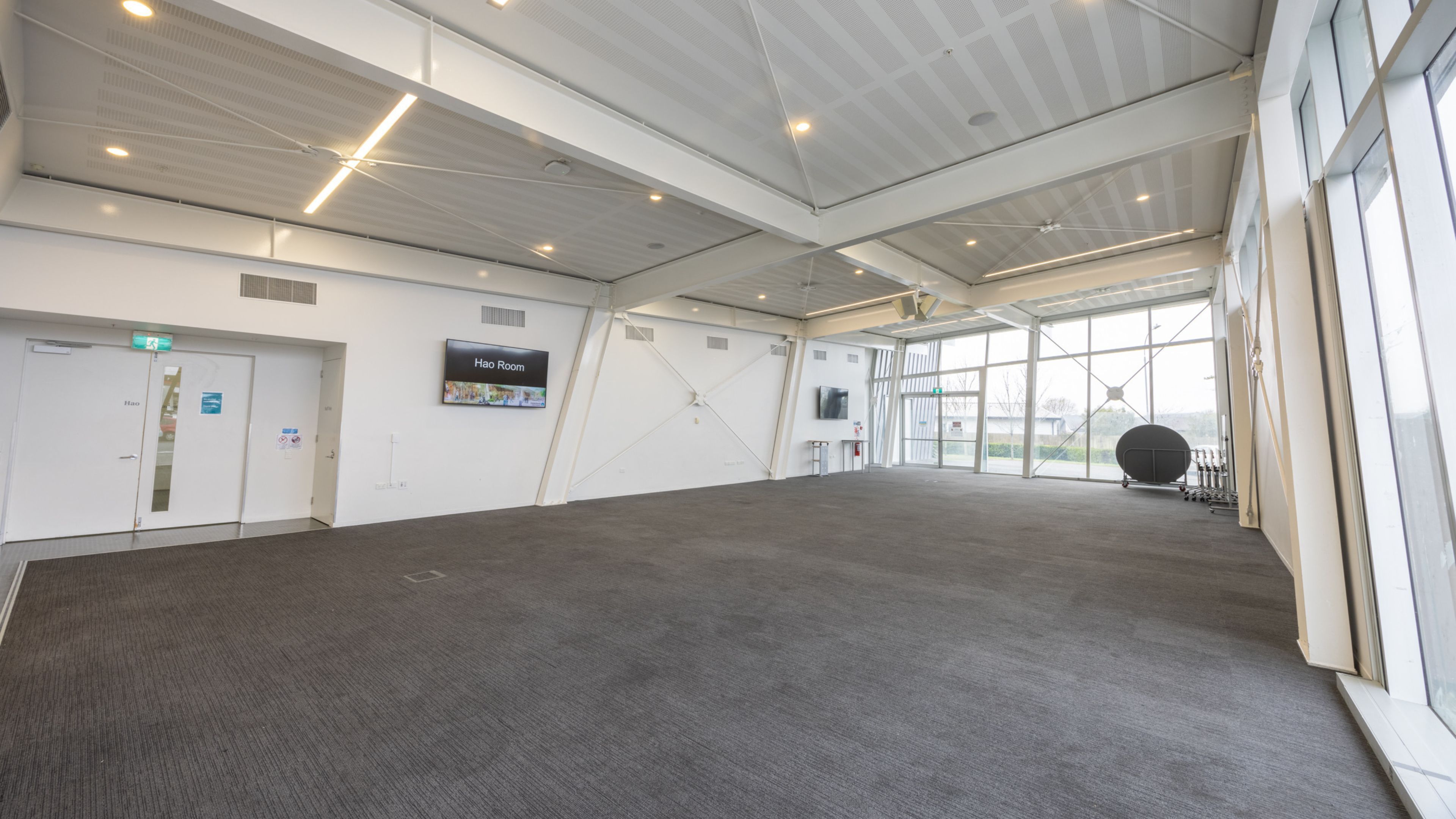 Large open hall with carpeted floor, angled ceiling and glazed wall