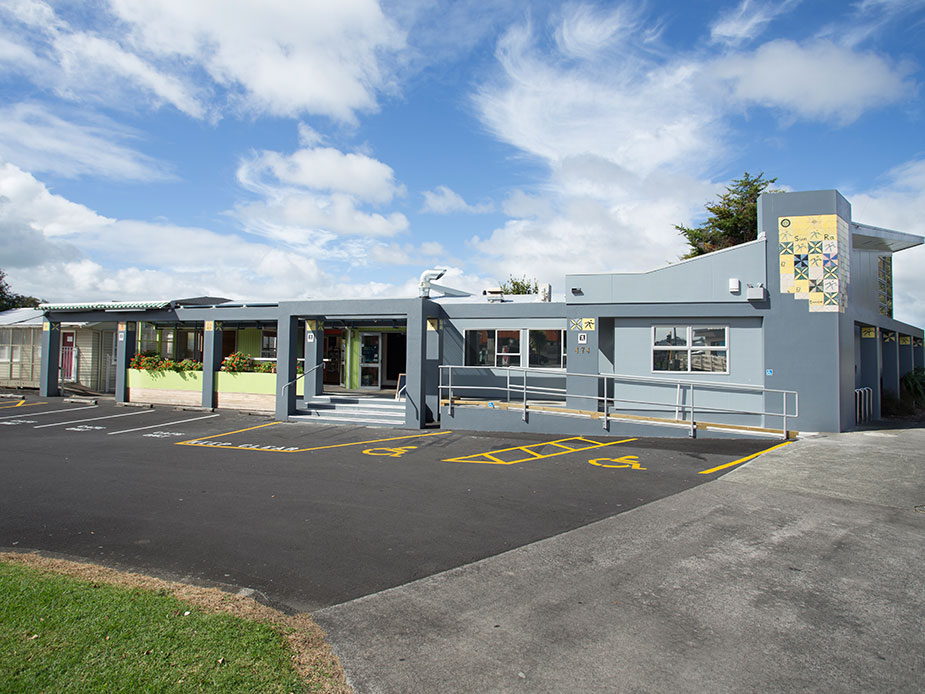 Single-storey blue community centre building with mural on fence, car park in front