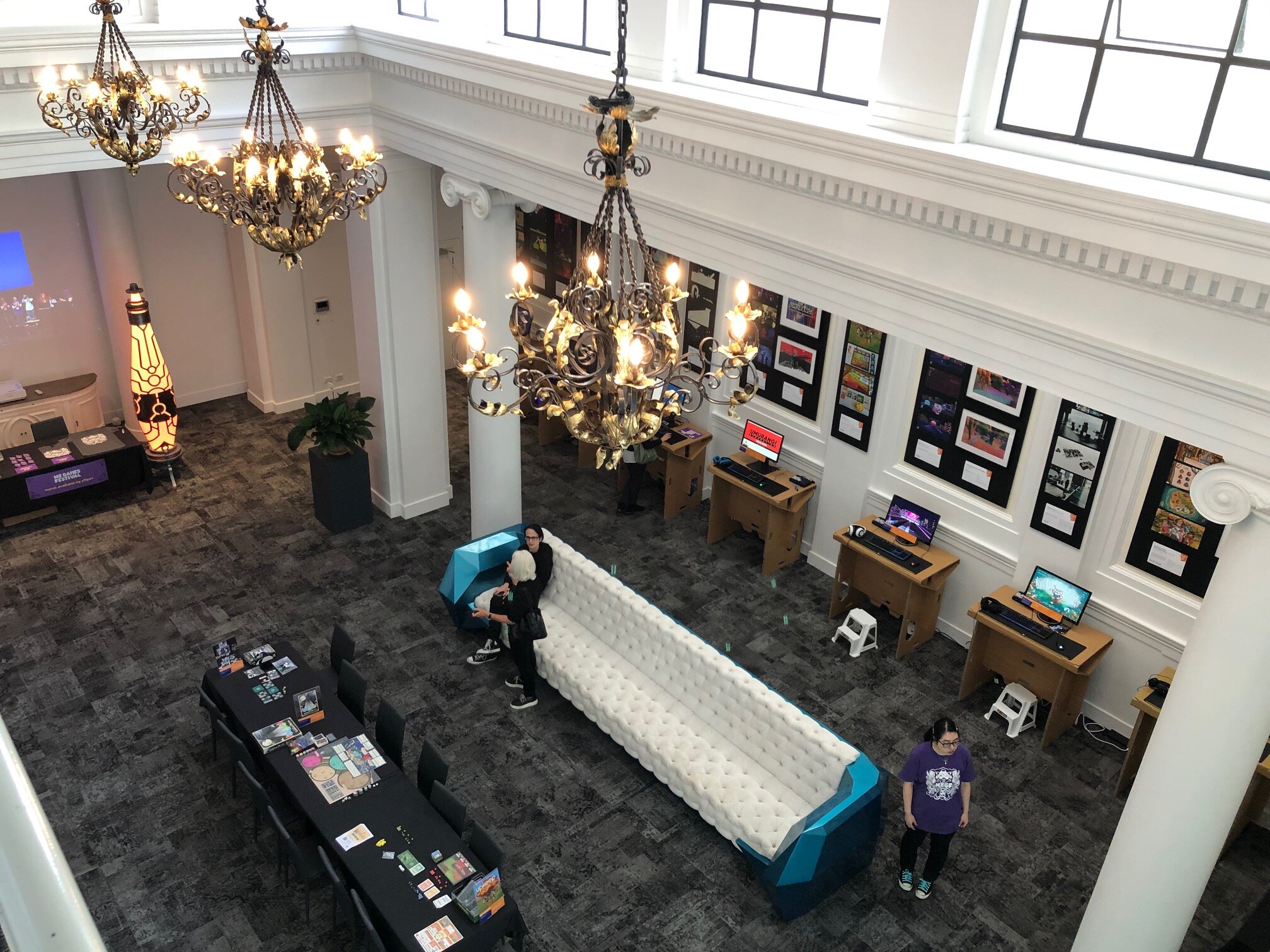 Grand hall viewed from a mezzanine with chandeliers, columns, and lounge furniture below