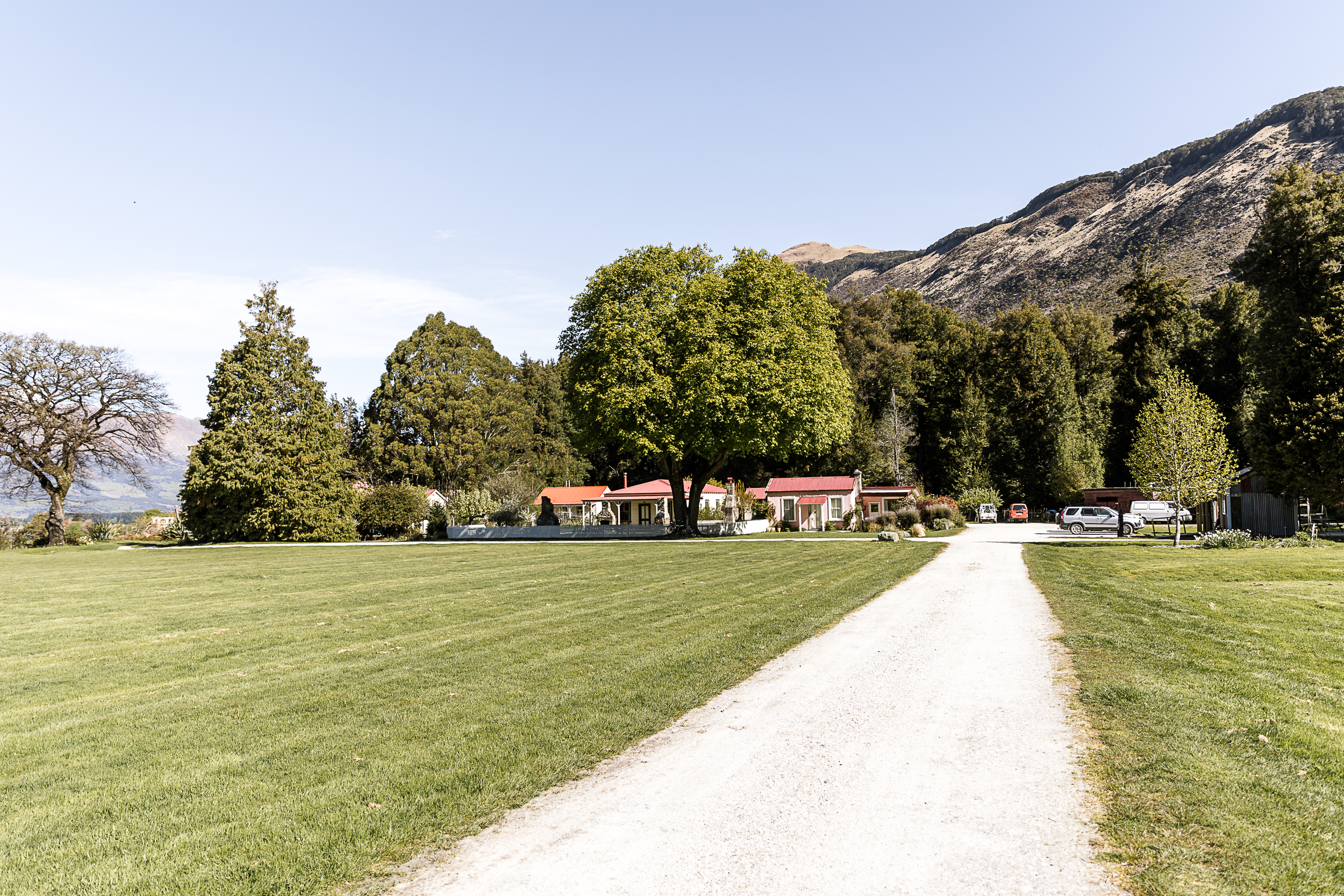 Gravel driveway leading to red-roofed cottages with mountains and trees in the background