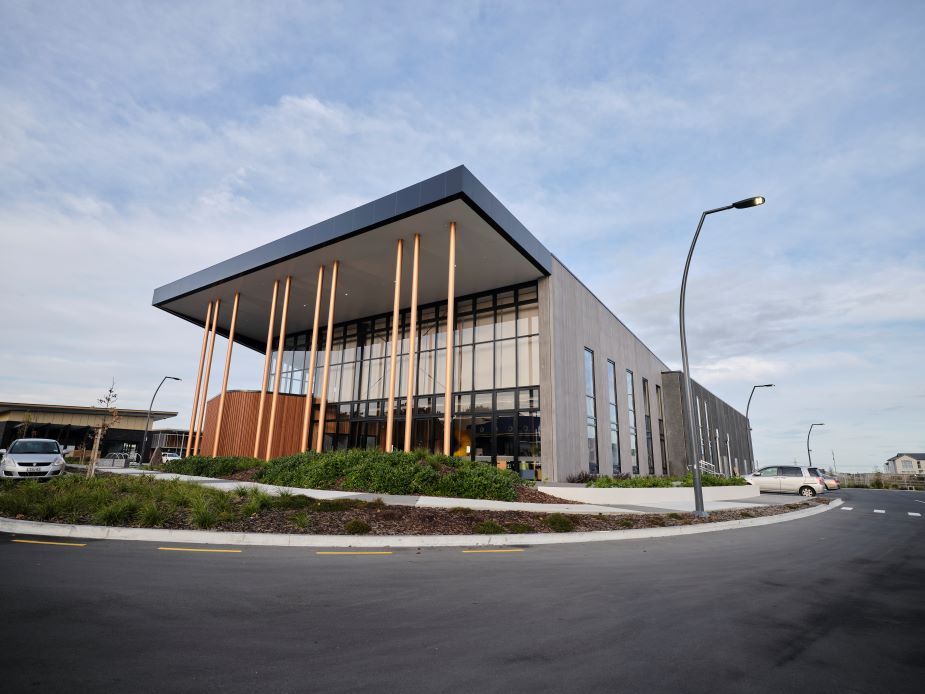 Contemporary building with glazed curtain wall, dark metal upper cladding, and bronze columns at entrance