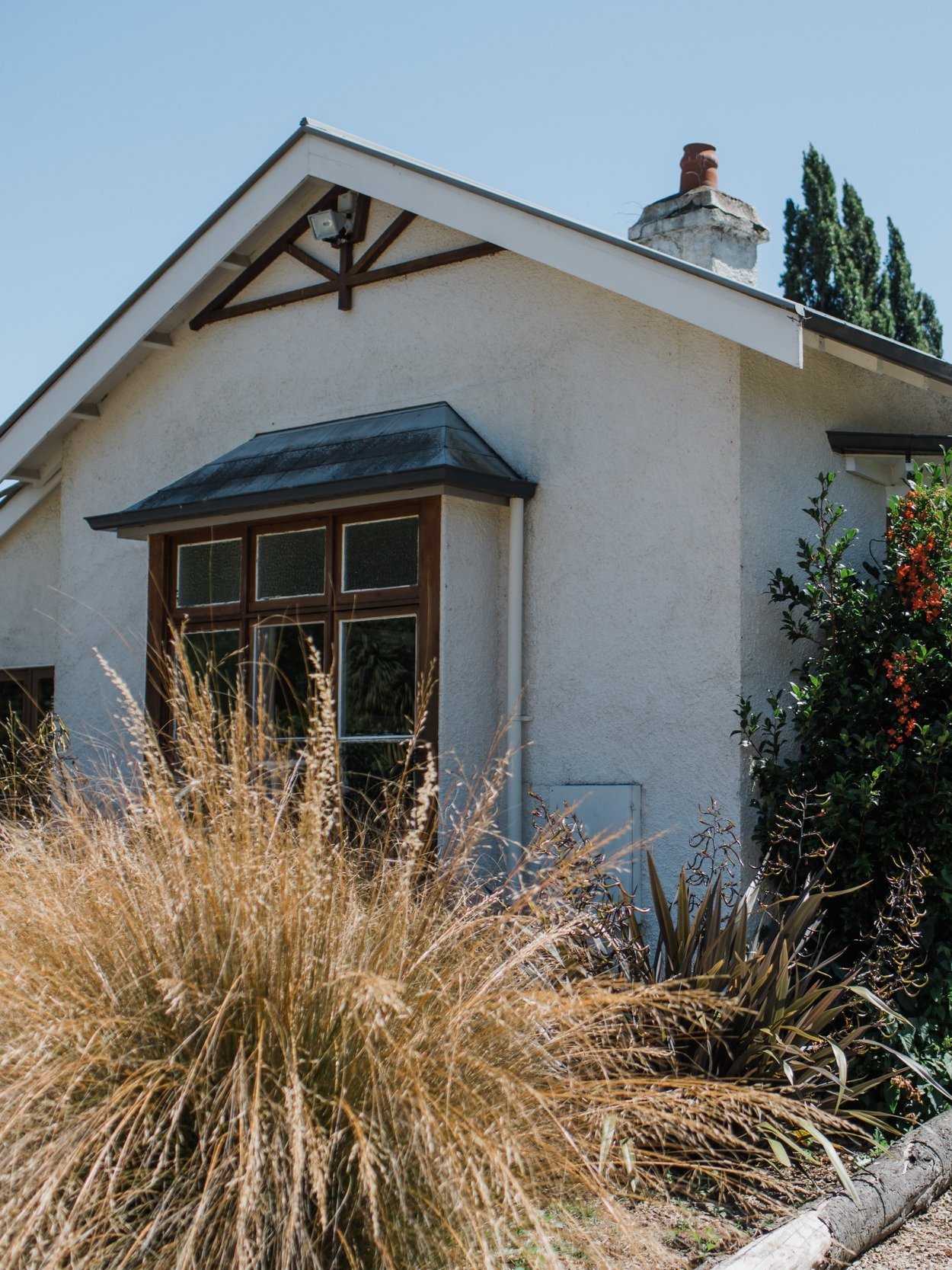 White rendered cottage exterior with chimney, ornamental grasses and shrubs in the foreground