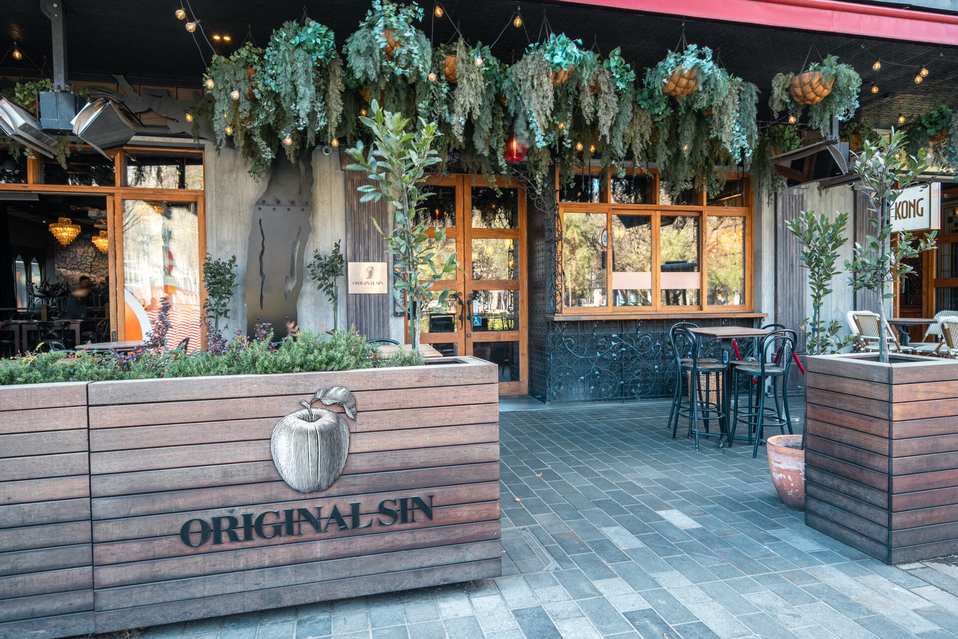 Restaurant exterior with hanging greenery, timber planter box with branding, and outdoor seating