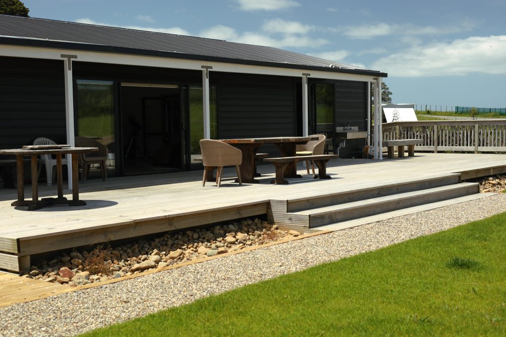 Dark-clad building with timber deck, outdoor furniture and lawn