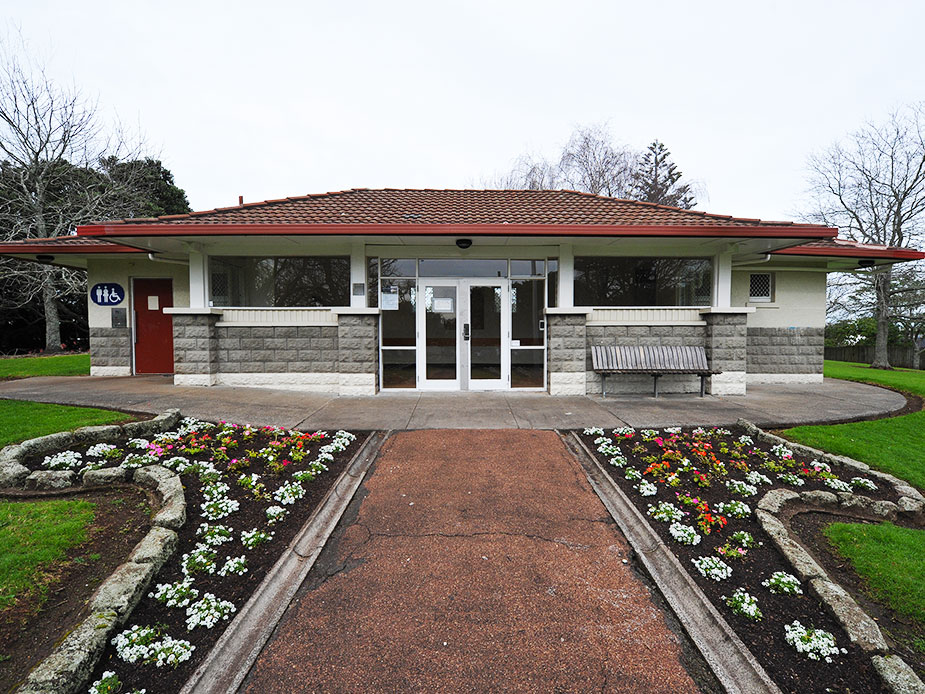 Front facade of low hall building with tiled roof, garden bed and entrance path
