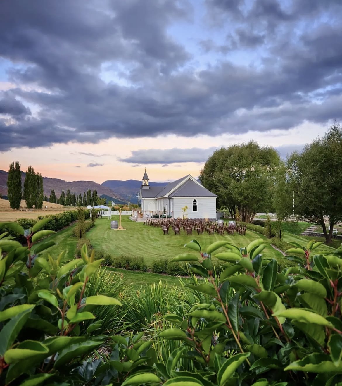 White church with bell tower set on a green lawn with mountains and dramatic sky behind