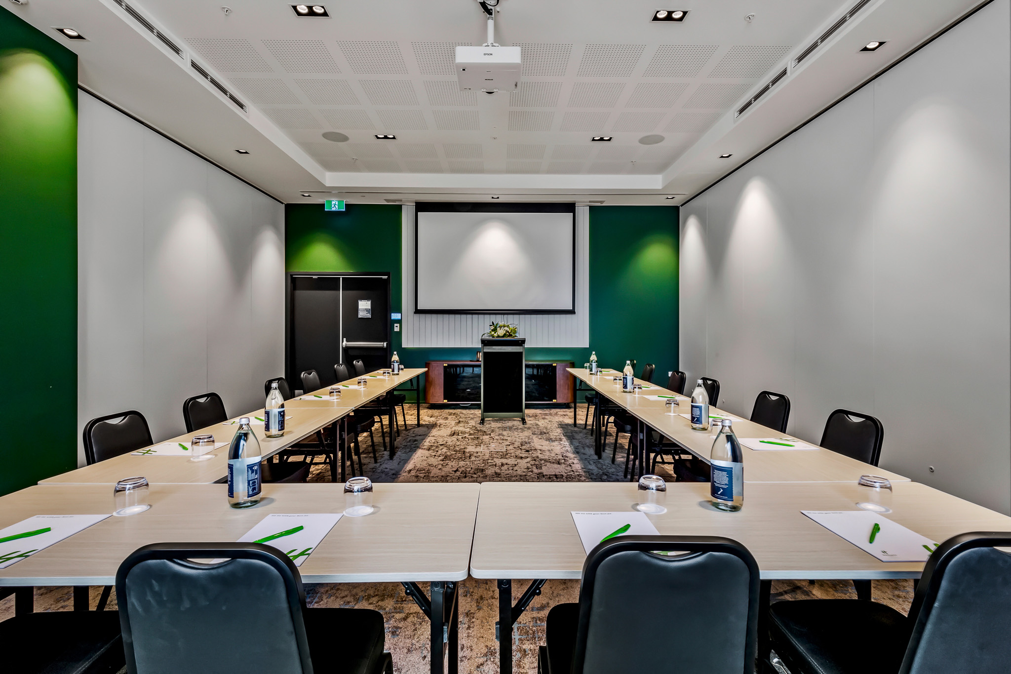 Meeting room in U-shape layout with green accent wall, projection screen, and patterned carpet