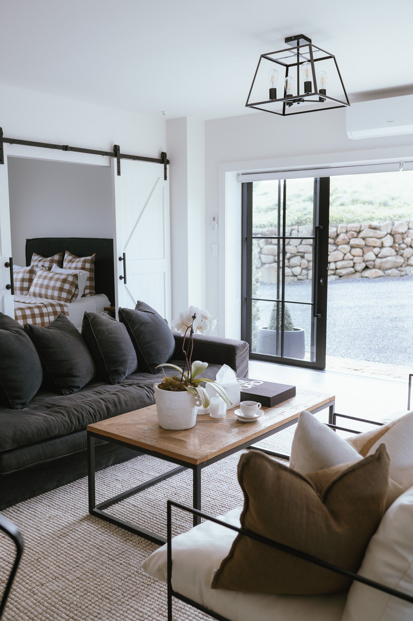 White interior sitting room with sliding barn door, dark sofa, and French doors to stone wall garden