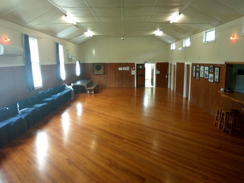 Plain hall interior with polished timber floor, panelled walls, and row seating