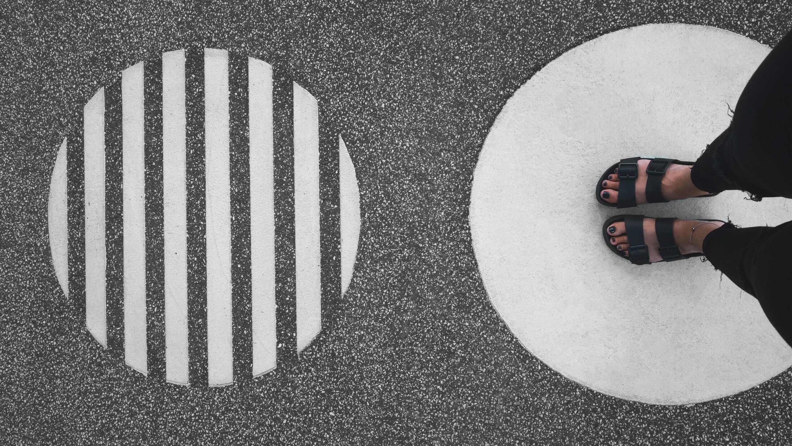 Overhead view of feet in sandals standing on painted circle markings on asphalt