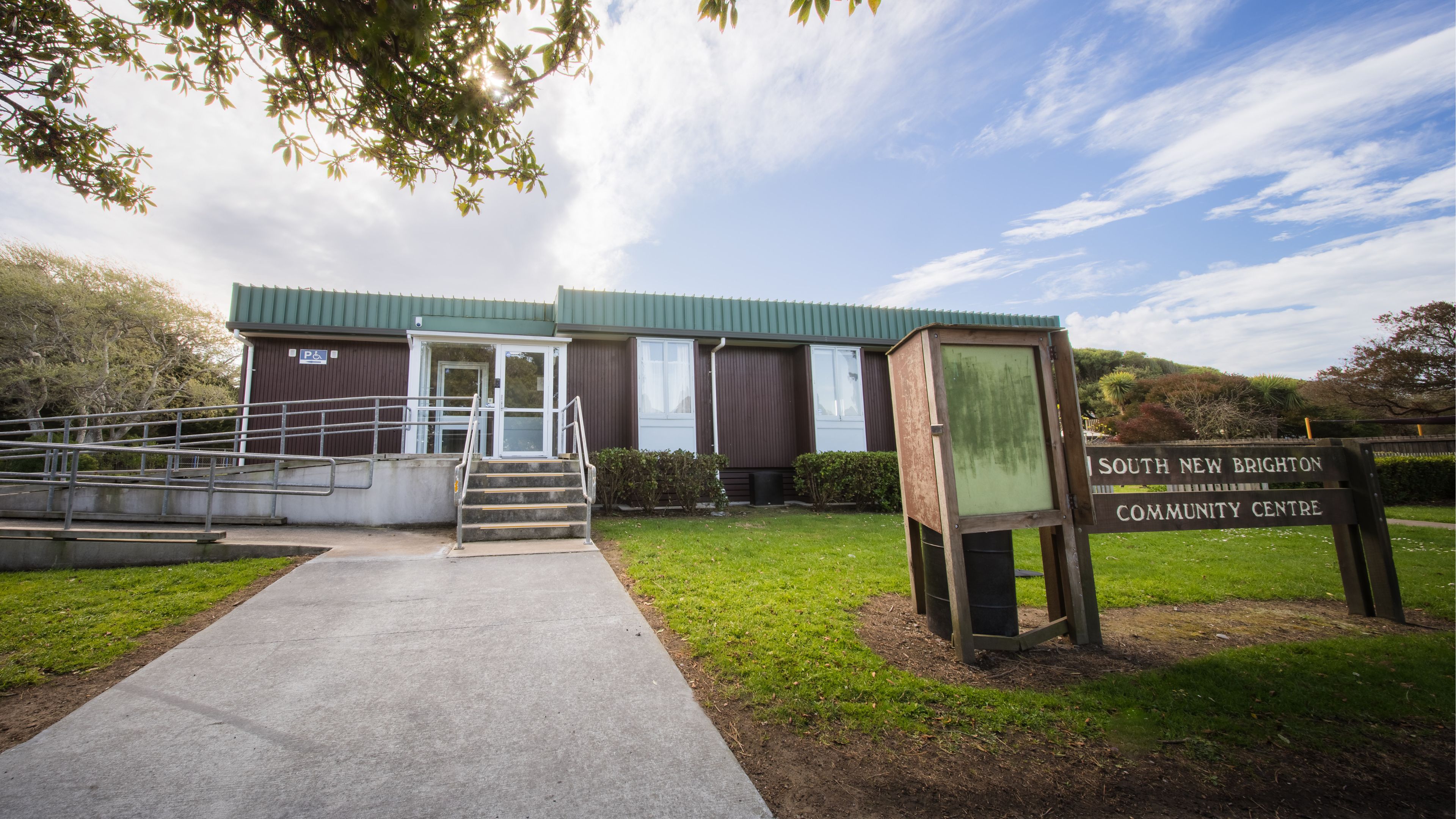 Single-storey community hall with green corrugated cladding and ramp entrance